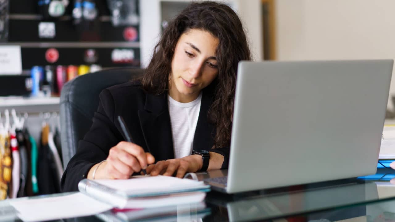 A woman sits at a table, deeply engrossed in writing, representing the concept of improved focus with the best mental supplement c60